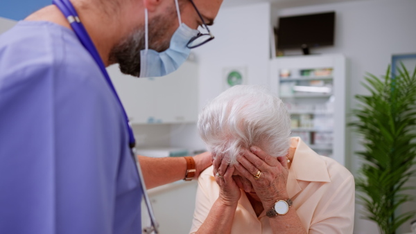 A doctor consoling sad senior woman patient during general check up in doctor's office.