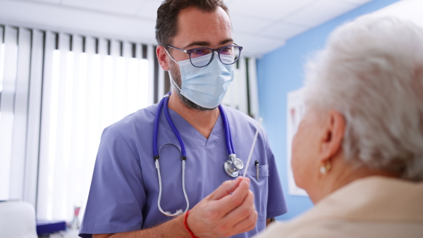 A doctor taking a nasal swab for coronavirus test from senior woman in his office.