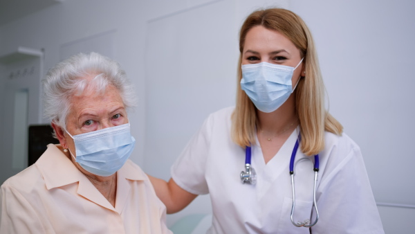 A young female doctor with elderly patient in examination room in clinic, coronavirus concept.