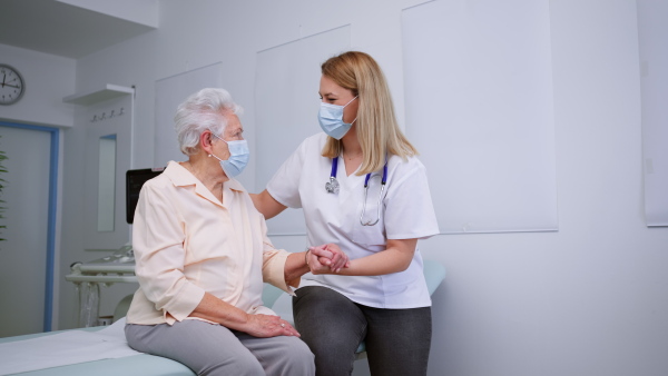 A young female doctor with elderly patient in examination room in clinic, coronavirus concept.