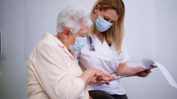 A young female doctor with elderly patient in examination room in clinic, coronavirus concept.