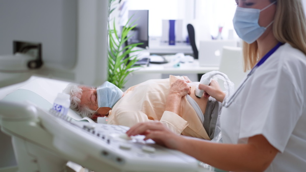 A young doctor is examining senior patient by using an ultrasound equipment in clinic.