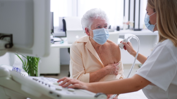 A young doctor is examining senior woman by using an ultrasound equipment in clinic.