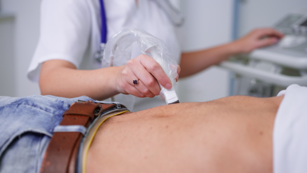 A close-up of doctor is examining mature man by using an ultrasound equipment in clinic.