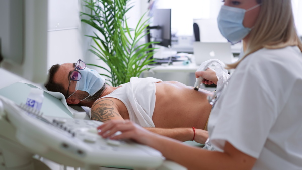 A young doctor is examining mature man by using an ultrasound equipment in clinic.