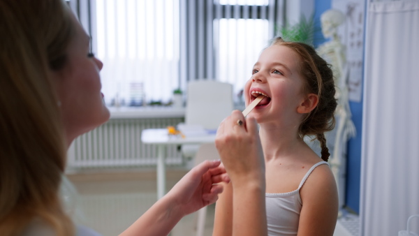 A zoung male doctor checking little girl's throat in his office.