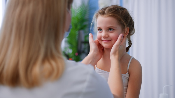 A young male doctor checking little girl's tonsils in his office.