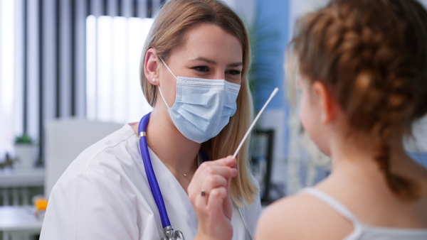 A young female doctor taking nasal swab test from little girl in clinic.