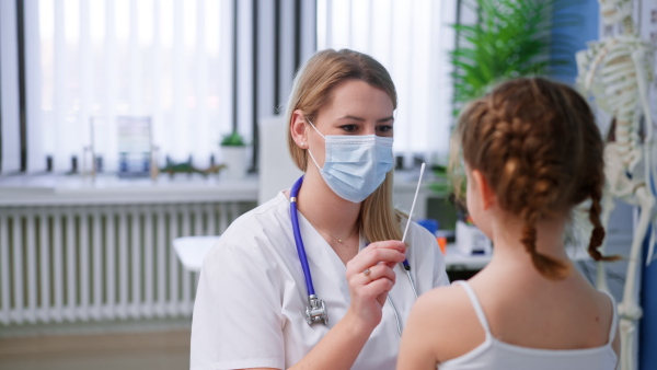 A young female doctor taking nasal swab test from little girl in clinic.