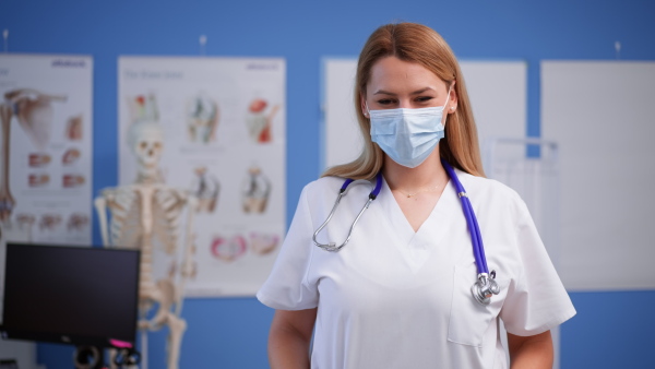 A young female doctor with face mask looking at camera in her office.