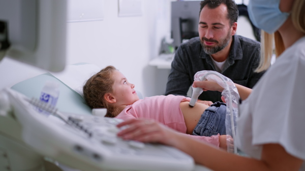 A young doctor is examining little girl by using an ultrasound equipment in clinic.