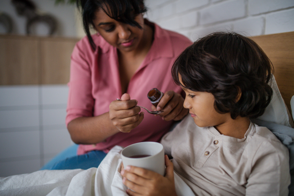 An ill boy taking medicine from his mother at home.