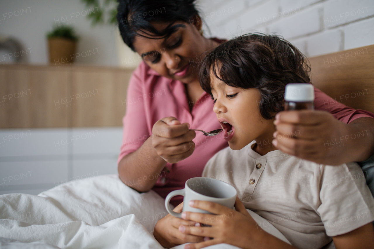 An ill boy taking medicine from his mother at home.