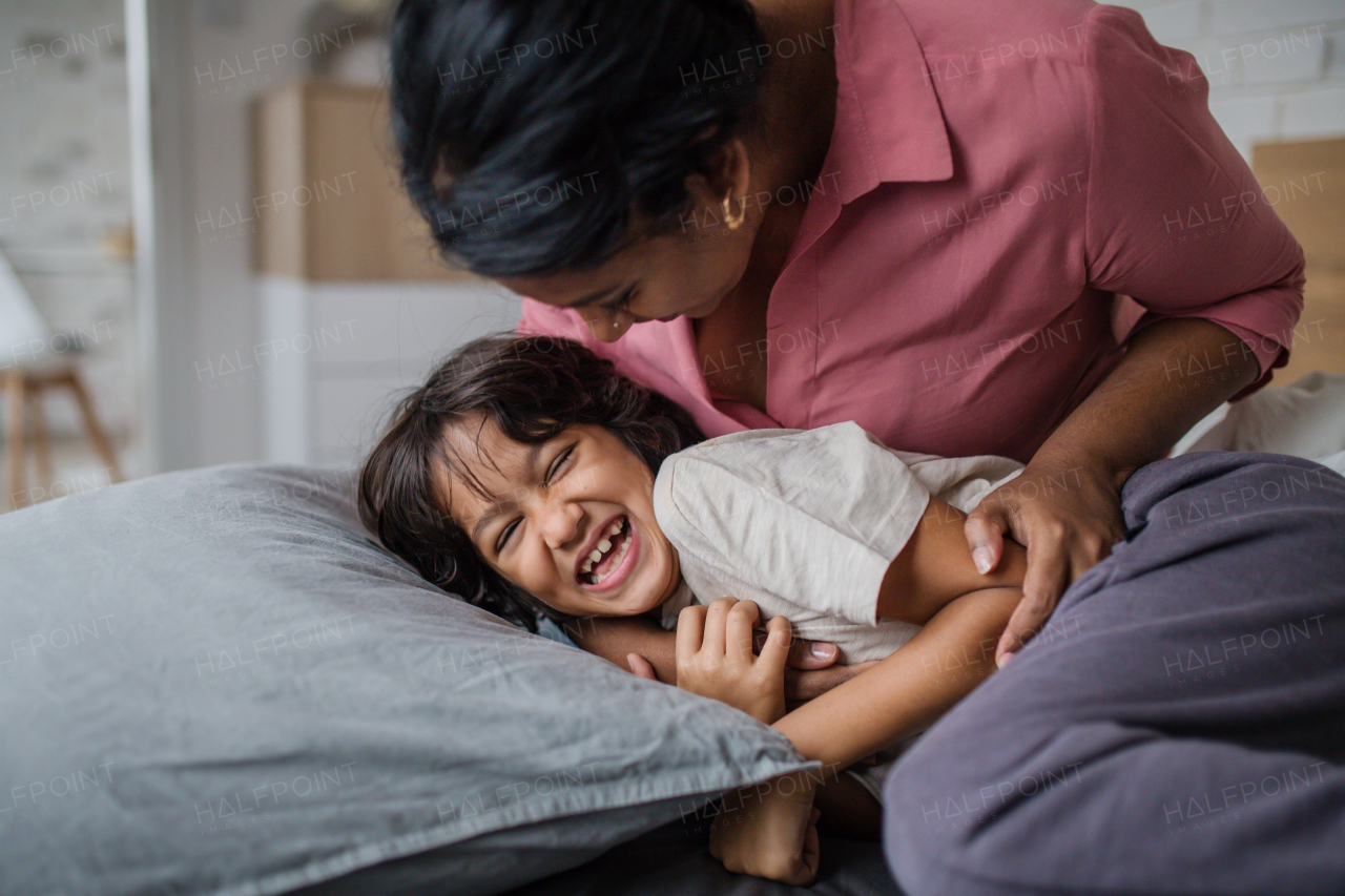 A happy mother tickling her little son when waking him up in morning.