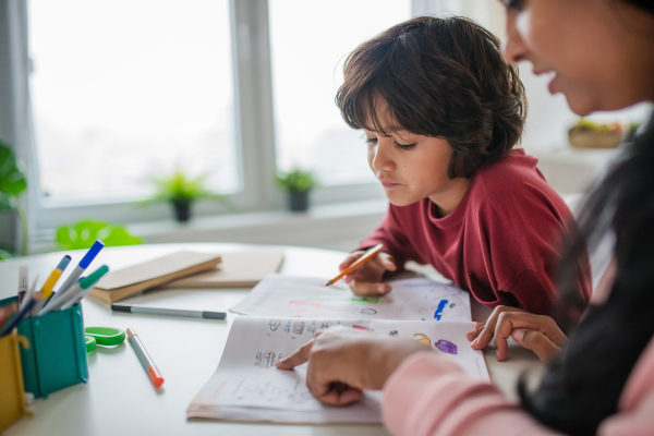 A little multiracial boy doing homework with his mother at home.