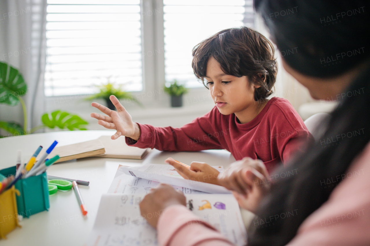 A little multiracial boy doing homework with his mother at home.