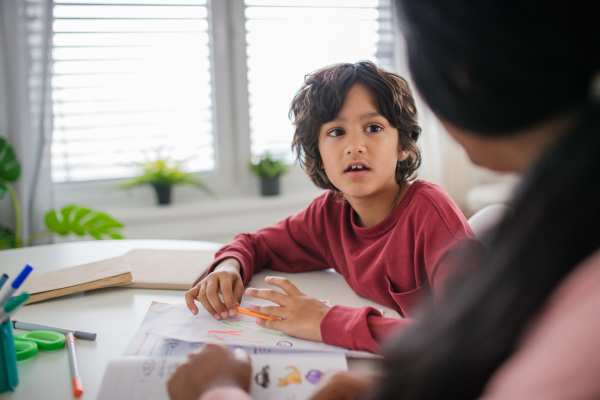 A little multiracial boy doing homework with his mother at home.