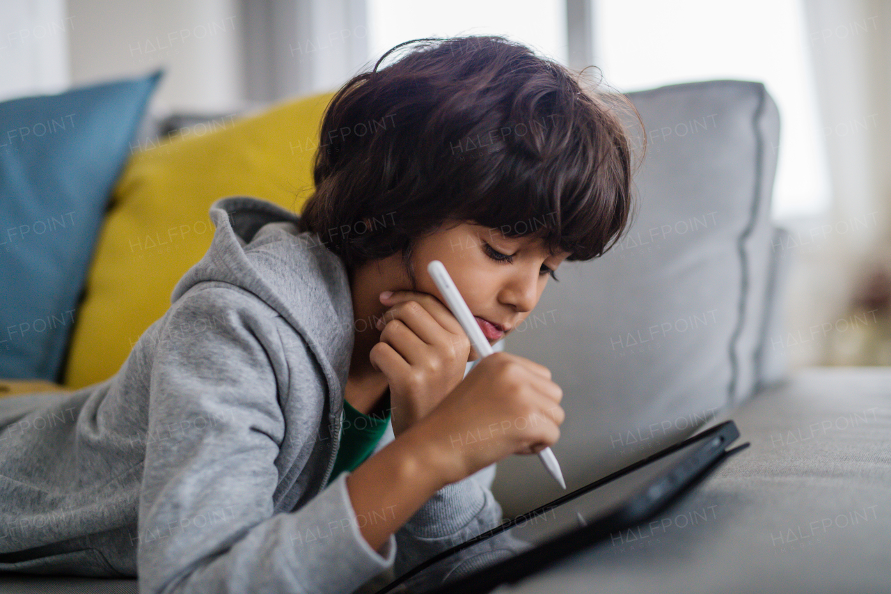 A little multiracial boy with tablet lying on sofa at home.