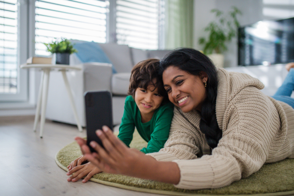 An Indian mother lying on floor with her little son at home, taking selfie.