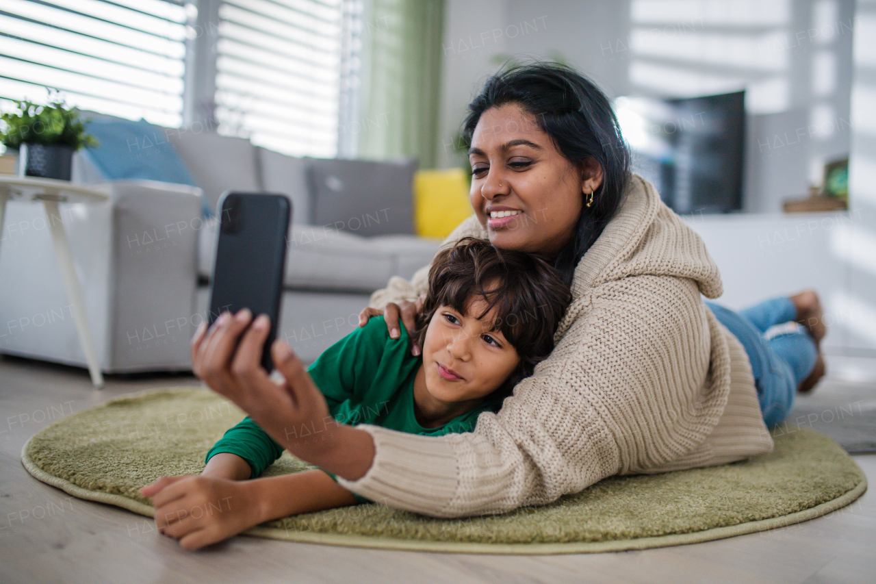 An Indian mother lying on floor with her little son at home, taking selfie.