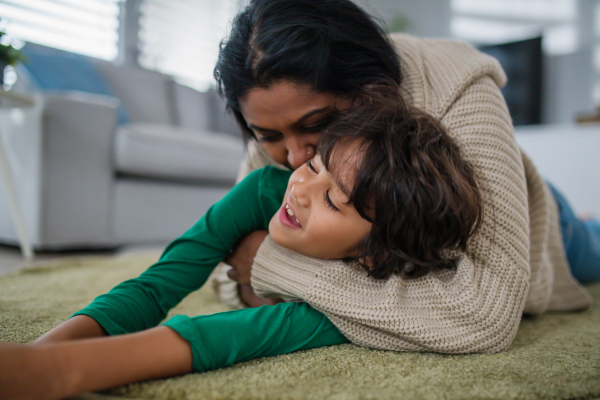 An Indian mother lying on floor and having fun with her little son at home.