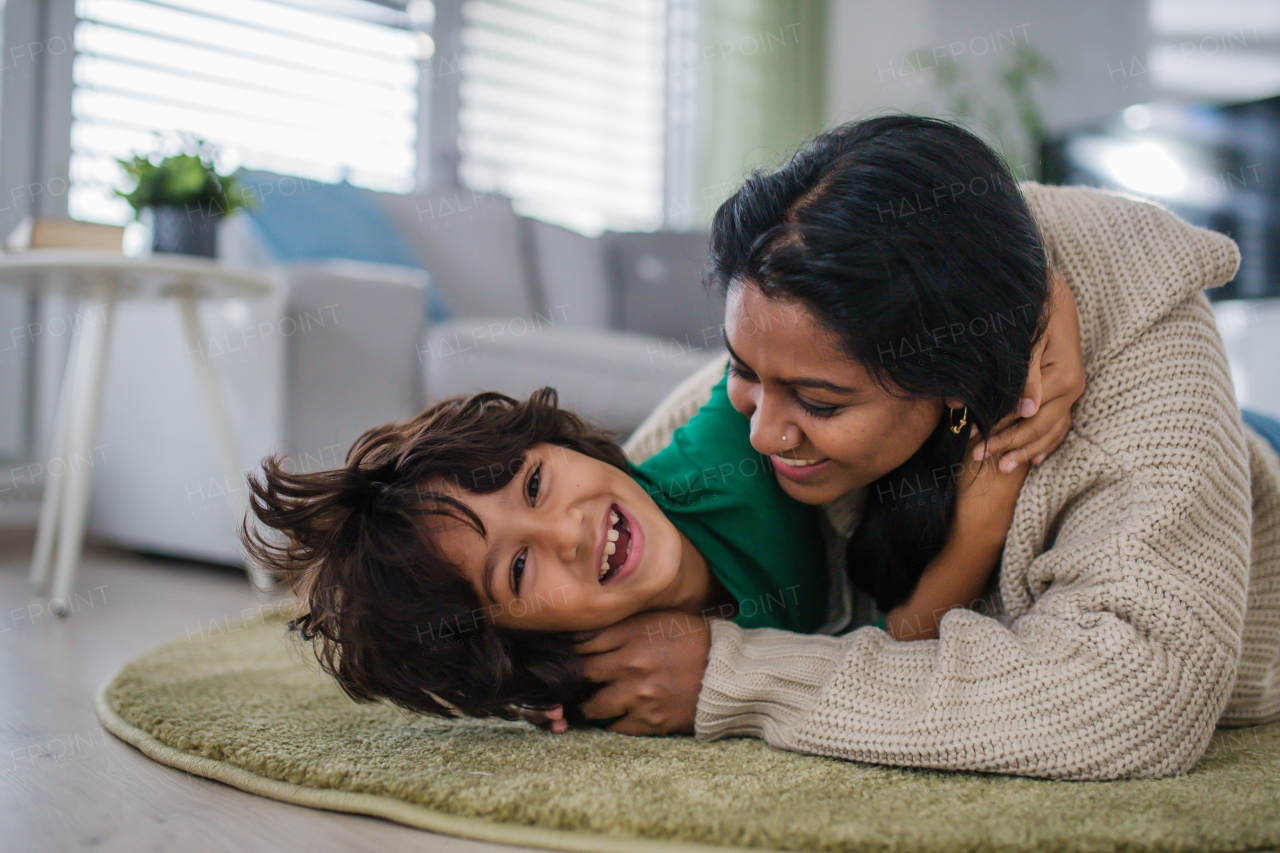 An Indian mother lying on floor and having fun with her little son at home, looking at camera.