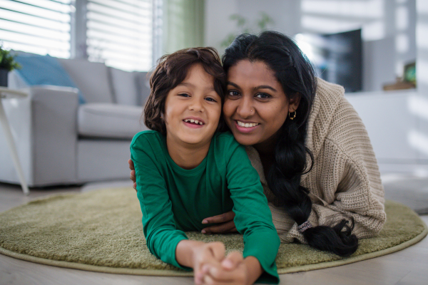 An indian mother lying on floor with her little son at home, looking at camera.