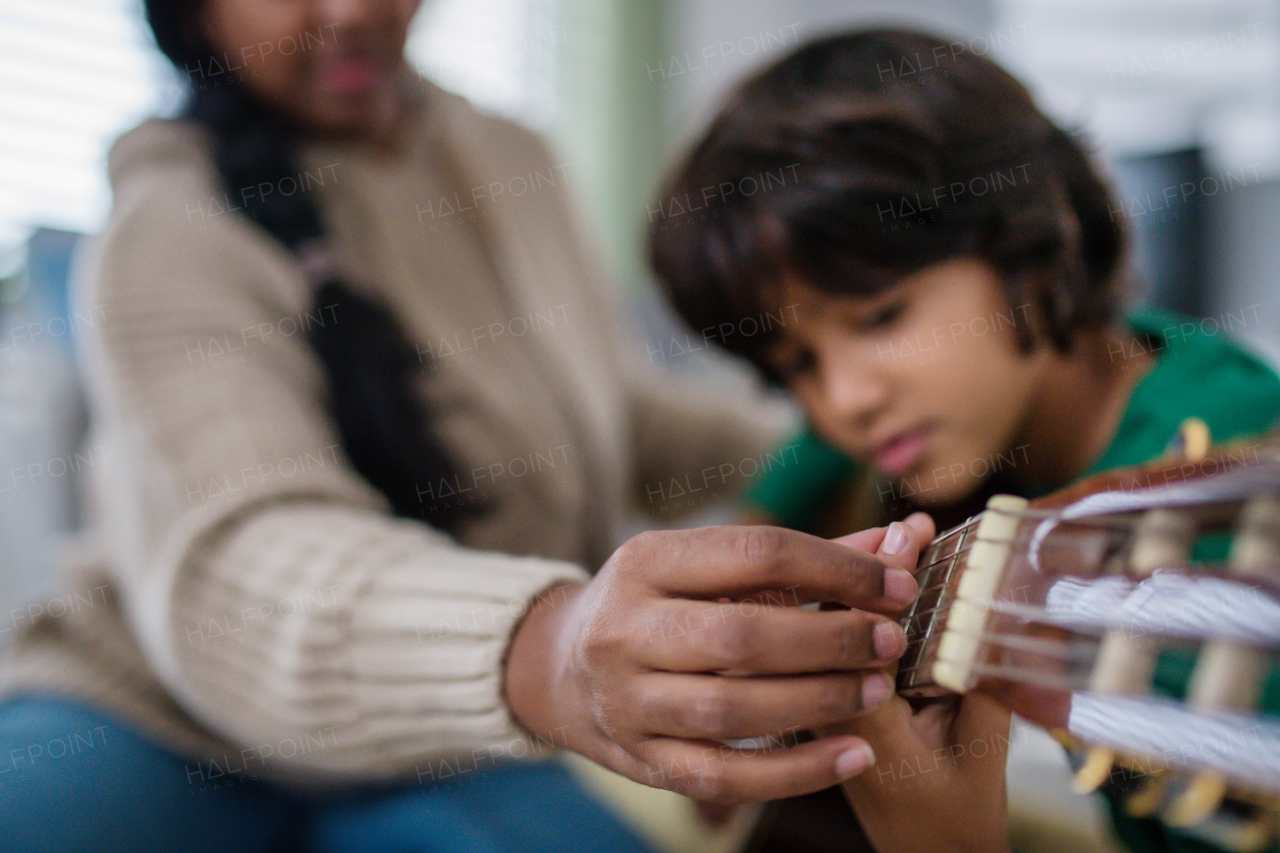 A little multiracial boy learning to play the guitar with his mother at home.