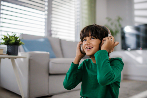 A happy multiracial boy with headphones listening to music at home.