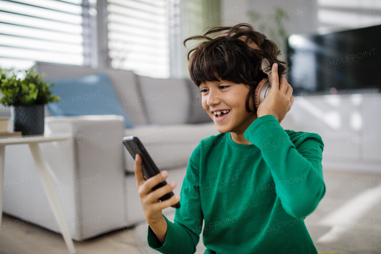 A happy multiracial boy with headphones and smartphone listening to music at home.