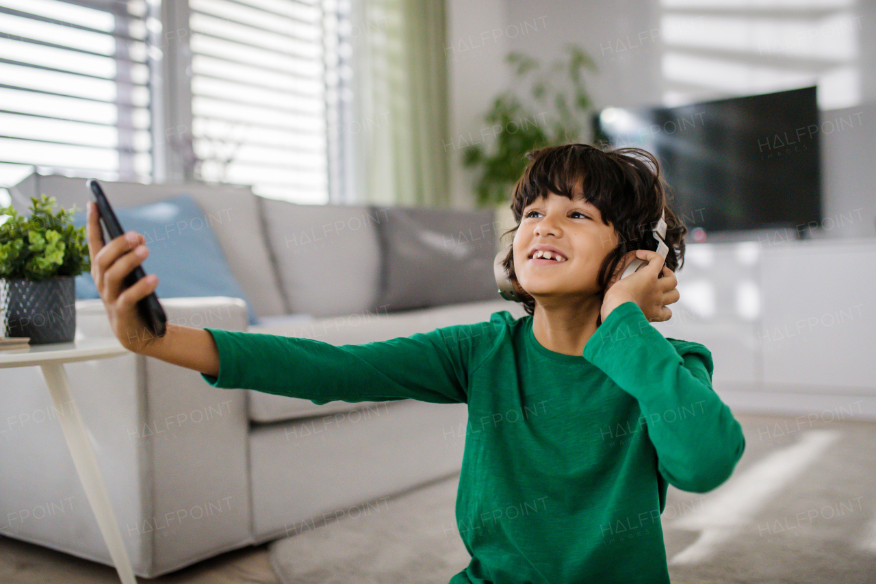 A happy multiracial boy with headphones and smartphone listening to music at home.