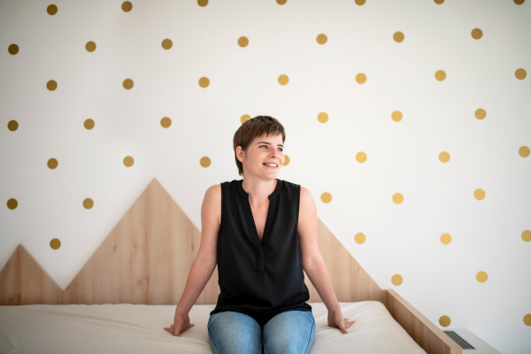 Front view of young happy woman sitting on bed in bedroom indoors at home.