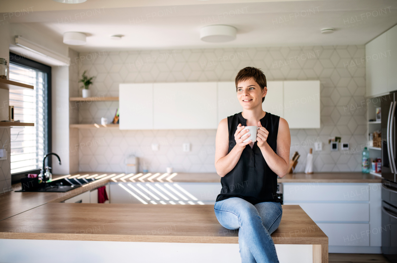 Front view of young woman with coffee sitting indoors at home. Copy space.