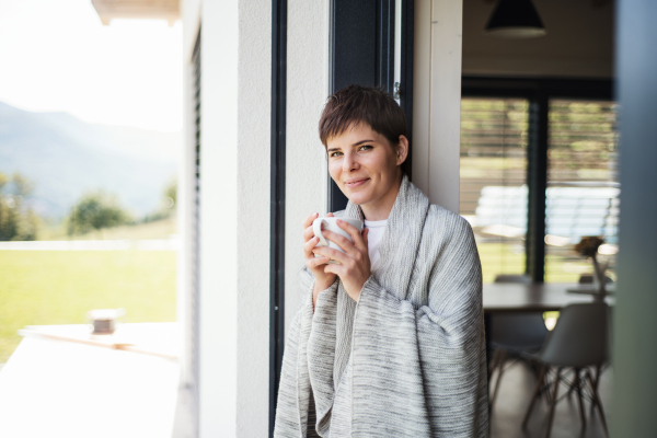 A young woman with coffee standing by patio door at home. Copy space.