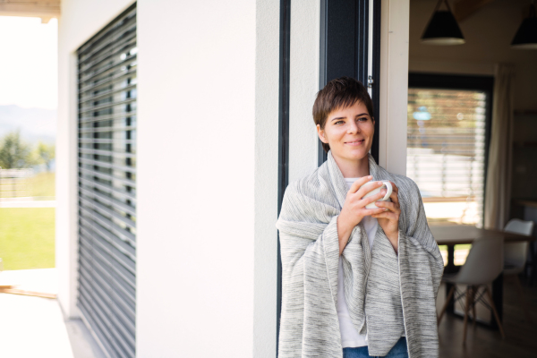 A young woman with coffee standing by patio door at home. Copy space.