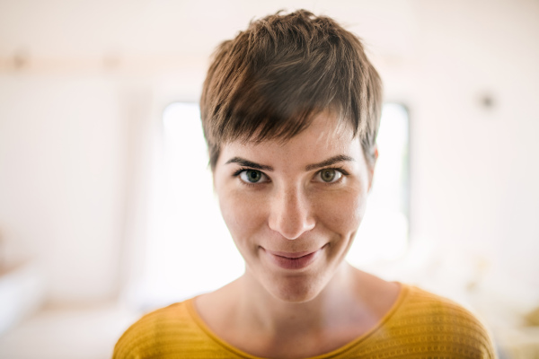 A front view of young woman standing indoors at home, close-up.