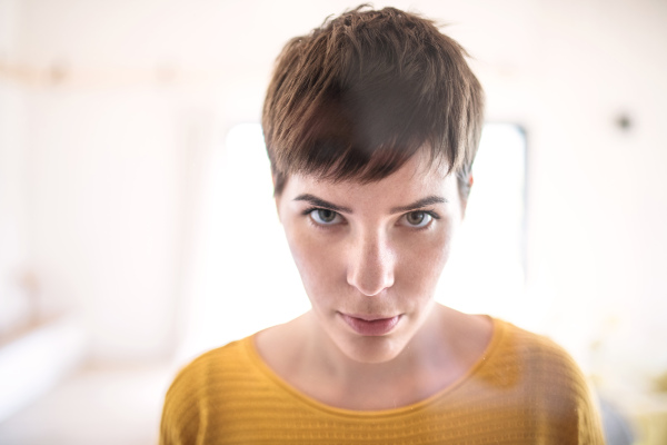 Front view of young woman standing indoors at home, close-up. Shot through glass.