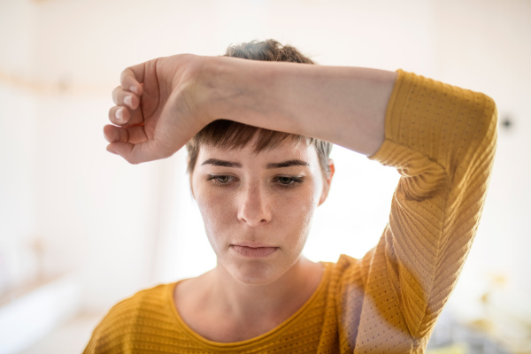 Front view of sad young woman standing indoors at home, close-up. Shot through glass.