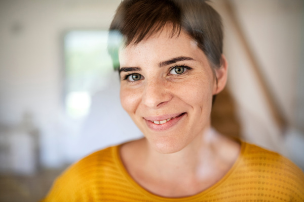 Front view of young woman standing indoors at home, close-up. Shot through glass.