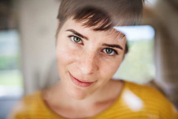 Front view of young woman standing indoors at home, close-up. Shot through glass.