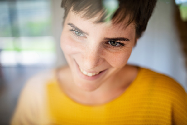 Front view of young woman standing indoors at home, close-up. Shot through glass.