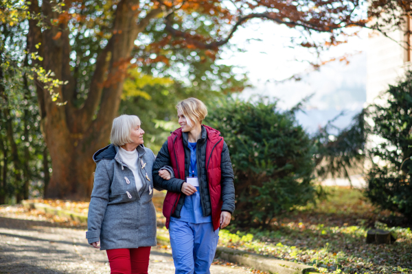 Front view of senior woman and caregiver outdoors on a walk in park, talking.