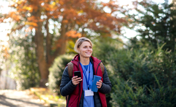 Portrait of woman caregiver, nurse or healthcare worker outdoors on the way to work, using smartphone.