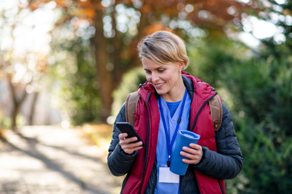 Portrait of woman caregiver, nurse or healthcare worker outdoors on the way to work, using smartphone.