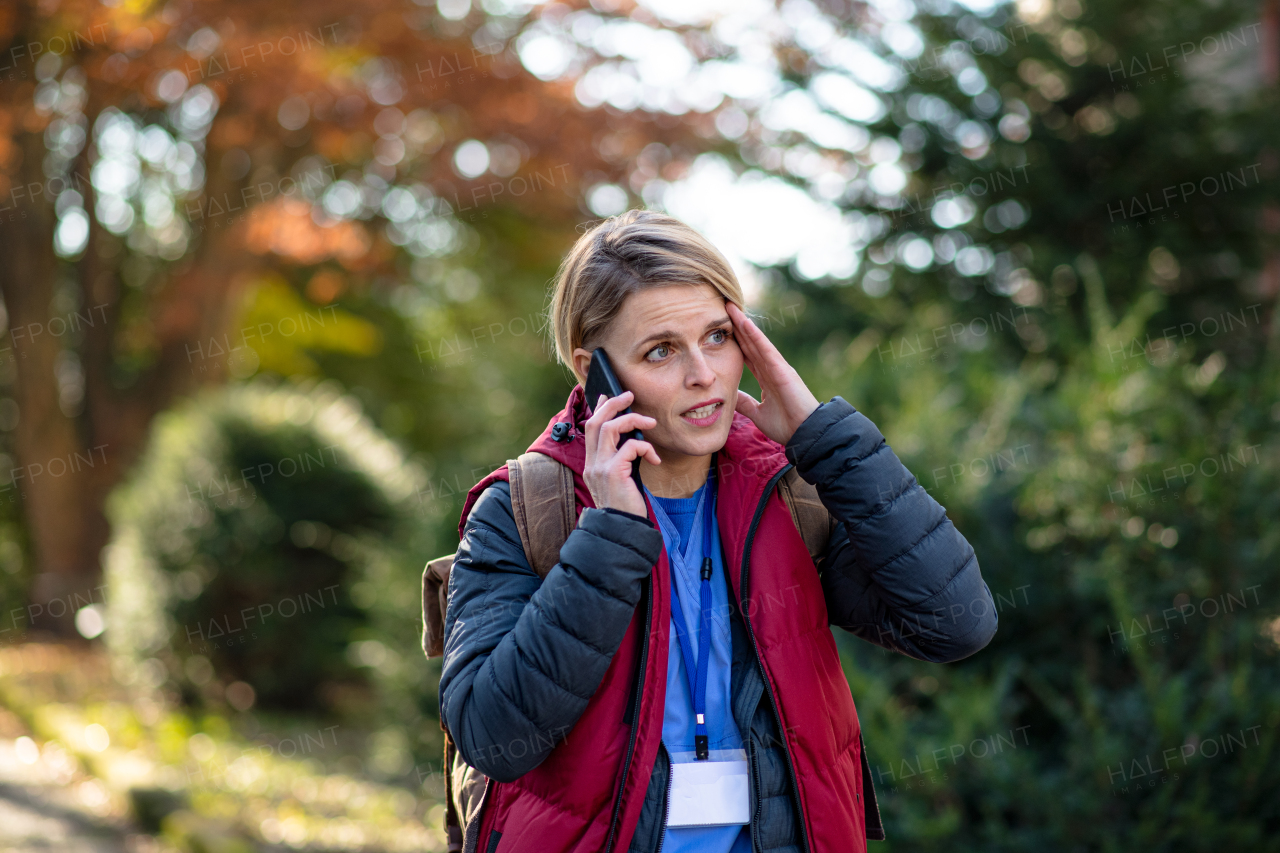 Portrait of woman caregiver, nurse or healthcare worker outdoors on the way to work, using smartphone.