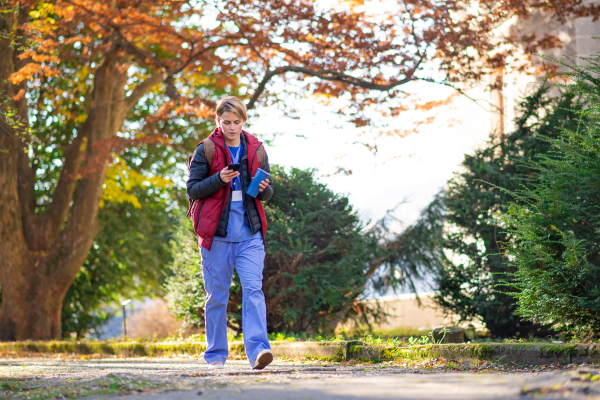 Portrait of woman caregiver, nurse or healthcare worker outdoors on the way to work, using smartphone.