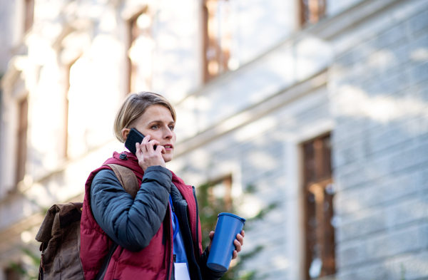 Portrait of woman caregiver, nurse or healthcare worker with smartphone outdoors on the way to work, coronavirus concept.