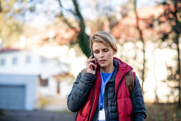 Portrait of woman caregiver, nurse or healthcare worker outdoors on the way to work, using smartphone.