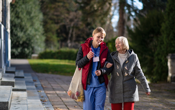 Front view of senior woman and caregiver outdoors on a walk in park, talking.