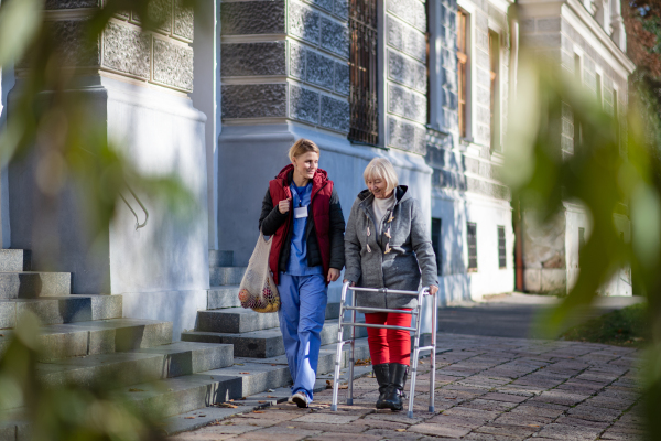 Happy senior woman with walking frame and caregiver outdoors in town, shopping and coronavirus concept.